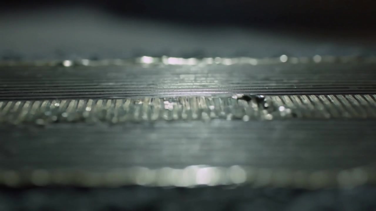 Riflessi mutevoli che si estendono su una striscia metallica scanalata a livello della strada, con un insetto che attraversa le scanalature.