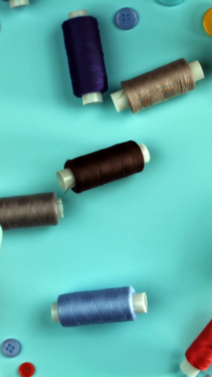 Colorful Sewing Threads and Buttons Falling on a Blue Background