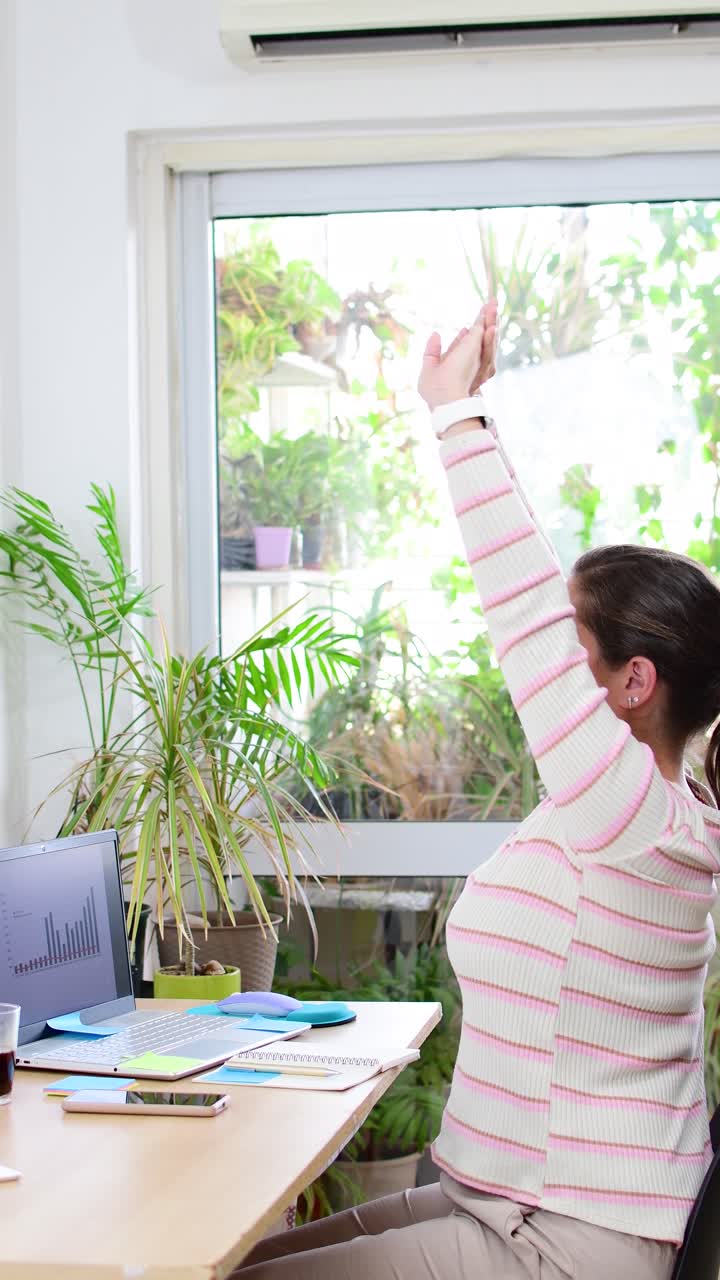 young lady during a break sitting by the table and stretching her arms from hard work
