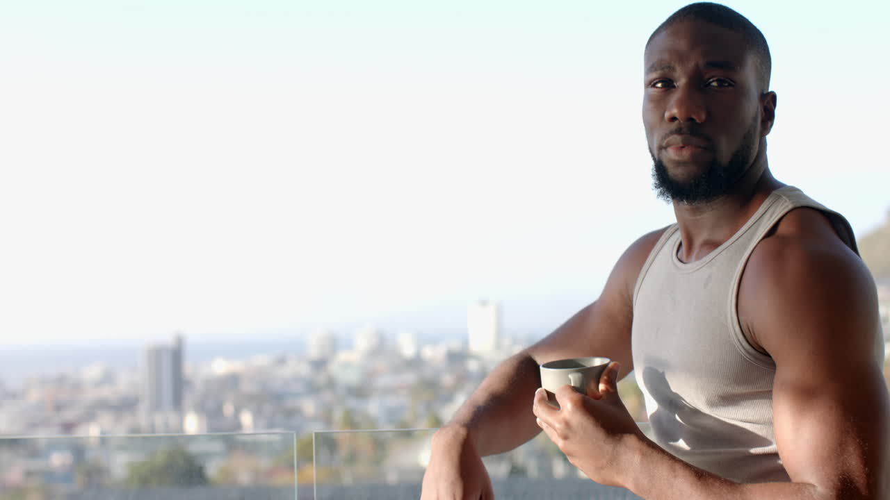 Strong and fit African American man holding cup, relaxing at home with city view