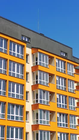 modern high-rise building against blue sky. newly built apartment building with colorful walls for urban residents. bright facade of multi storey city house. vertical video
