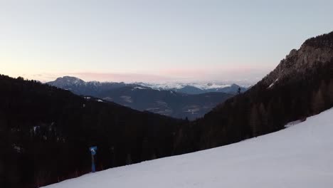 Excursionista-En-La-Cima-De-Una-Colina-Pista-De-Esquí-Vacía-Y-Nevada-Disfrutando-De-La-Vista-Del-Atardecer-De-La-Montaña-Revelan-Foto