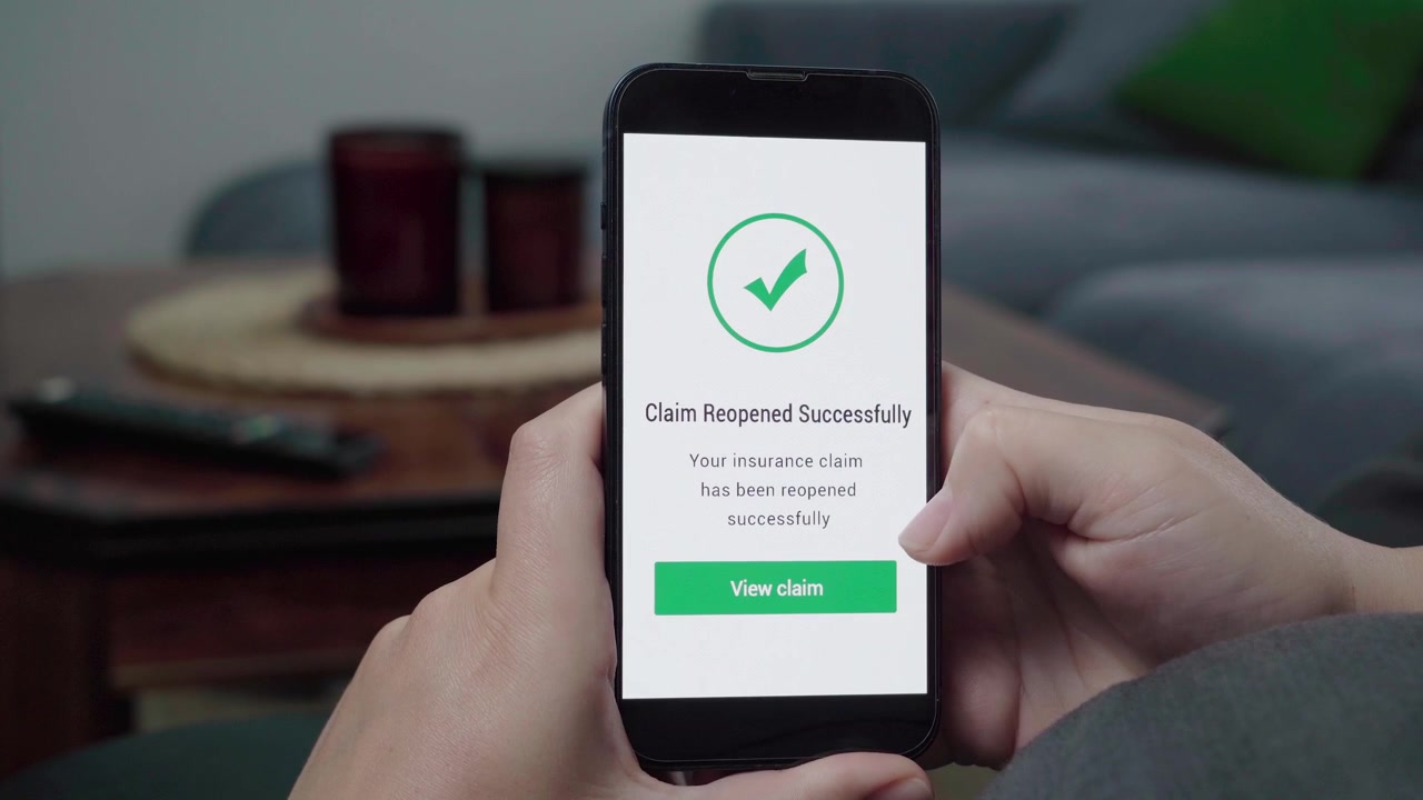 Una persona controlla un messaggio "Reclamo Riaperto con Successo" con un segno di spunta verde e un pulsante "Visualizza reclamo" su un'interfaccia telefonica di assicurazione digitale.