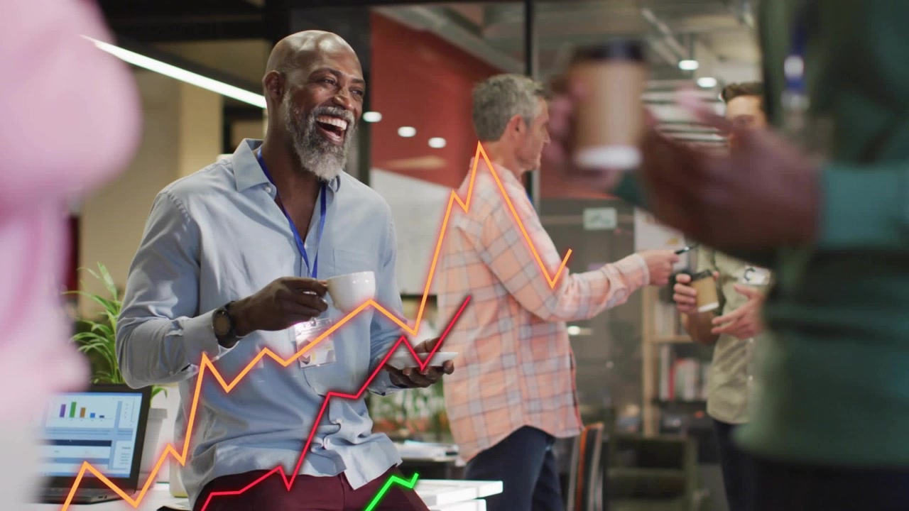 Sitting man laughing while team chatting and animated office graphs rising on laptop beside him