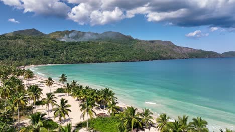 Aerial-flight-over-palm-trees-revealing-in-orbit-the-beach-of-La-Boca-del-Diablo,-Samaná,-Dominican-Republic