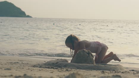 una chica bonita en traje de baño rosa construye un castillo de arena en la orilla del mar
