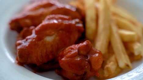 Alas-De-Pollo-De-Búfalo-Con-Papas-Fritas-Servidas-En-Un-Plato-Blanco