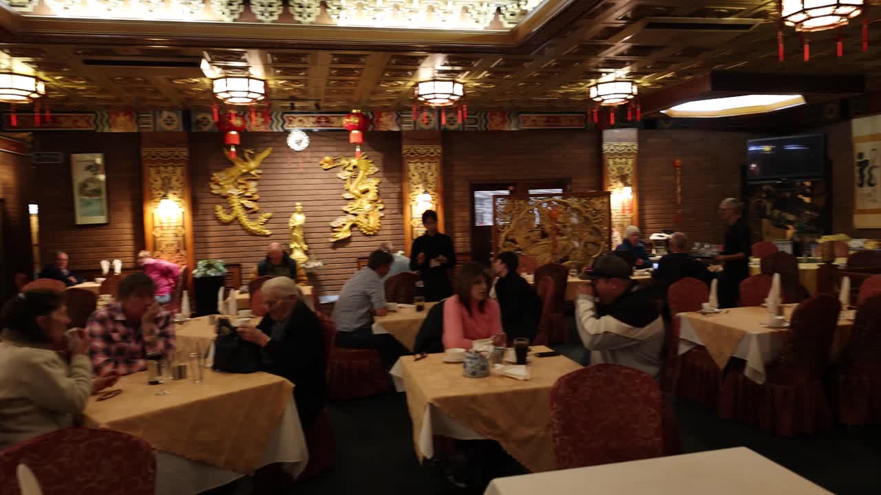 Warmly lit Chinese restaurant with ornate decor, inviting atmosphere, diners browsing menus, slow camera pan