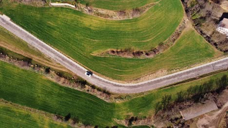 Nice-aerial-zenithal-shot-of-a-white-car-making-a-turn-on-a-green-country-road