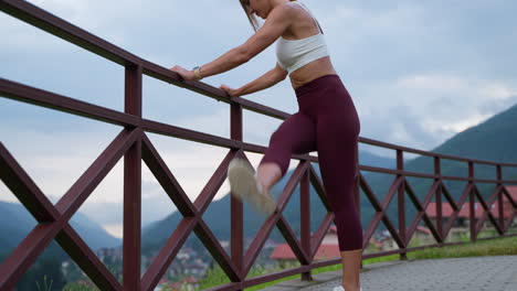 woman stretching outdoors by a fence in mountains