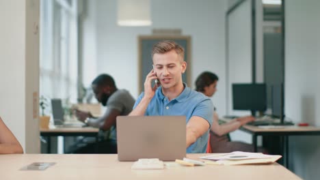 Young-man-talking-mobile-phone-at-office.-Smiling-guy-speaking-on-cellphone