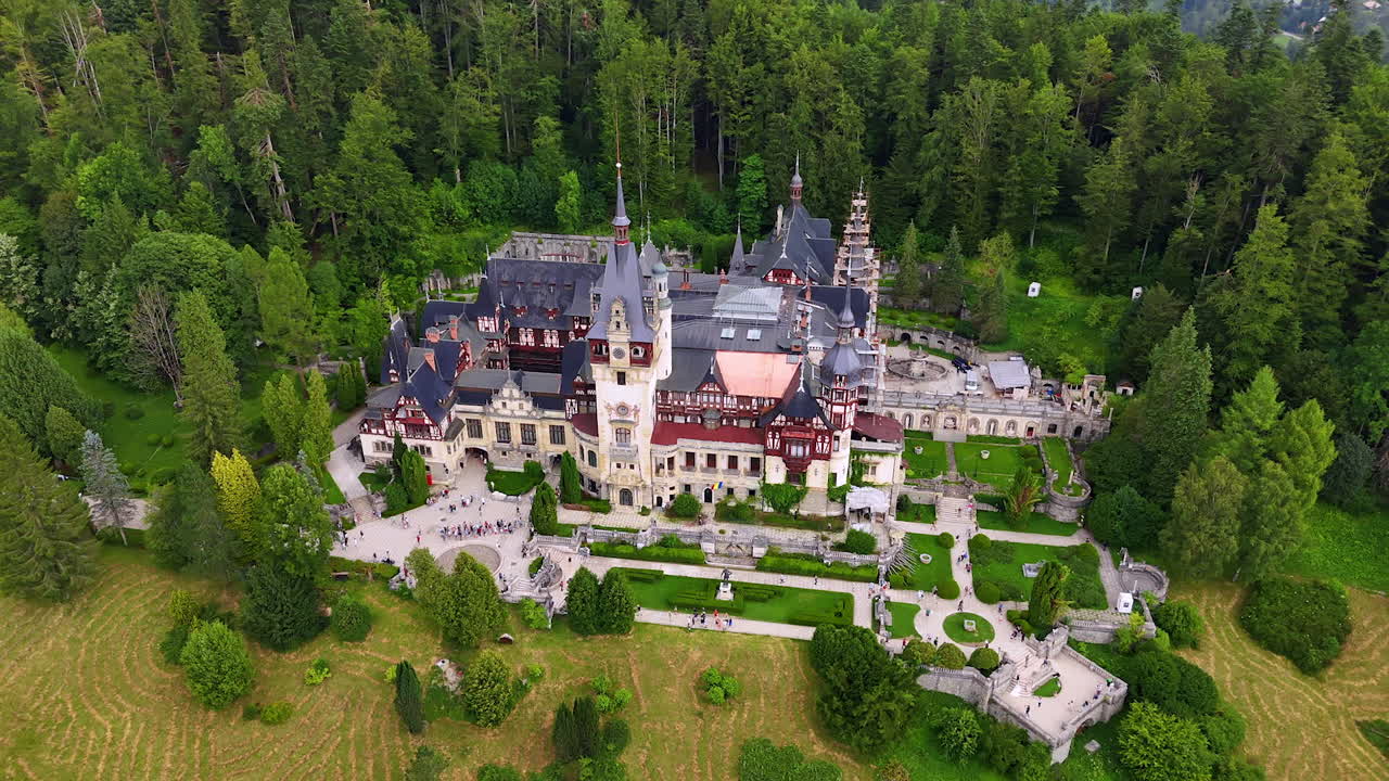 Breath-taking view of the famous Pele? Castle in the Carpathian Mountains, Romania. Lots of people walk by the territory of the landmark. Aerial view