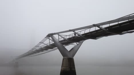 people crossing london's millennium bridge shrouded in heavy fog