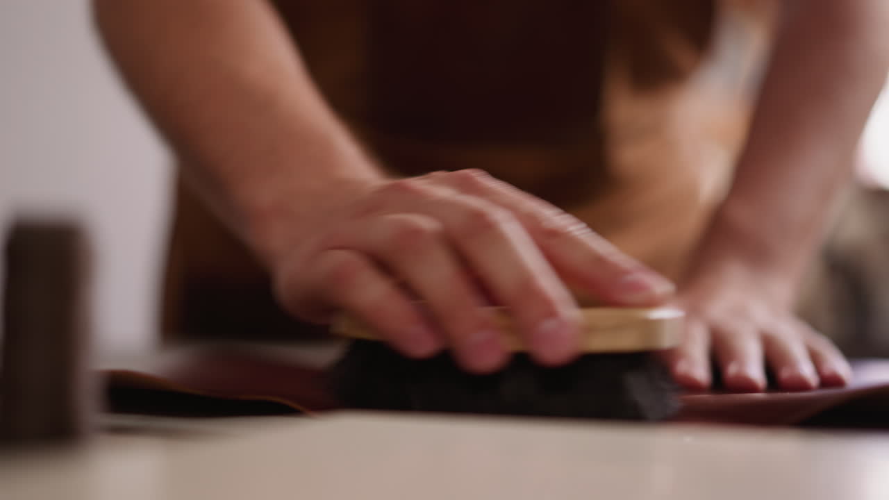 trabajador limpia una hoja de cuero con un pincel en la mesa en el taller