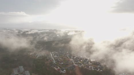 imágenes de drones de una urbanización en noruega con algo de niebla flotando en el aire y el sol iluminando las nubes