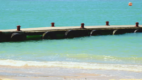 Niedriger-Steg-Mit-Pollern-Ragt-Ins-Klare,-Blaue-Meer-Mit-Plätschernden-Wellen,-Ruhig