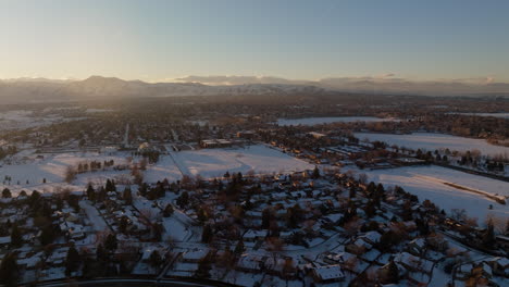 Drone-shot-of-the-sun-setting-over-the-Rocky-Mountains-in-Denver,-CO-on-a-snowy-winter-day