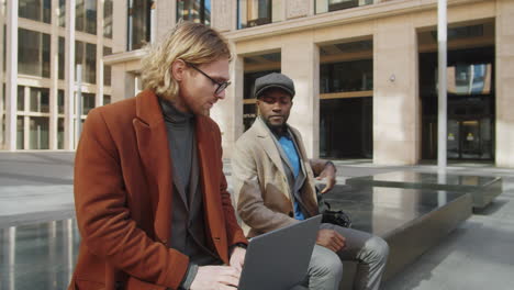 dos hombres de negocios multiétnicos hablando y usando computadora portátil al aire libre