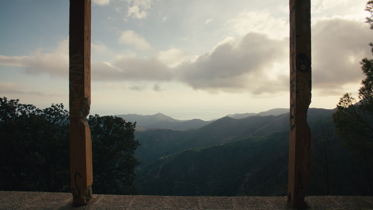 Una majestuosa vista a la montana y al mar se aprecia a través de dos pilares derruidos y cubiertos de grafitis de una villa abandonada. La luz suave y difusa del final de la tarde crea una atmósfera melancólica y poética.