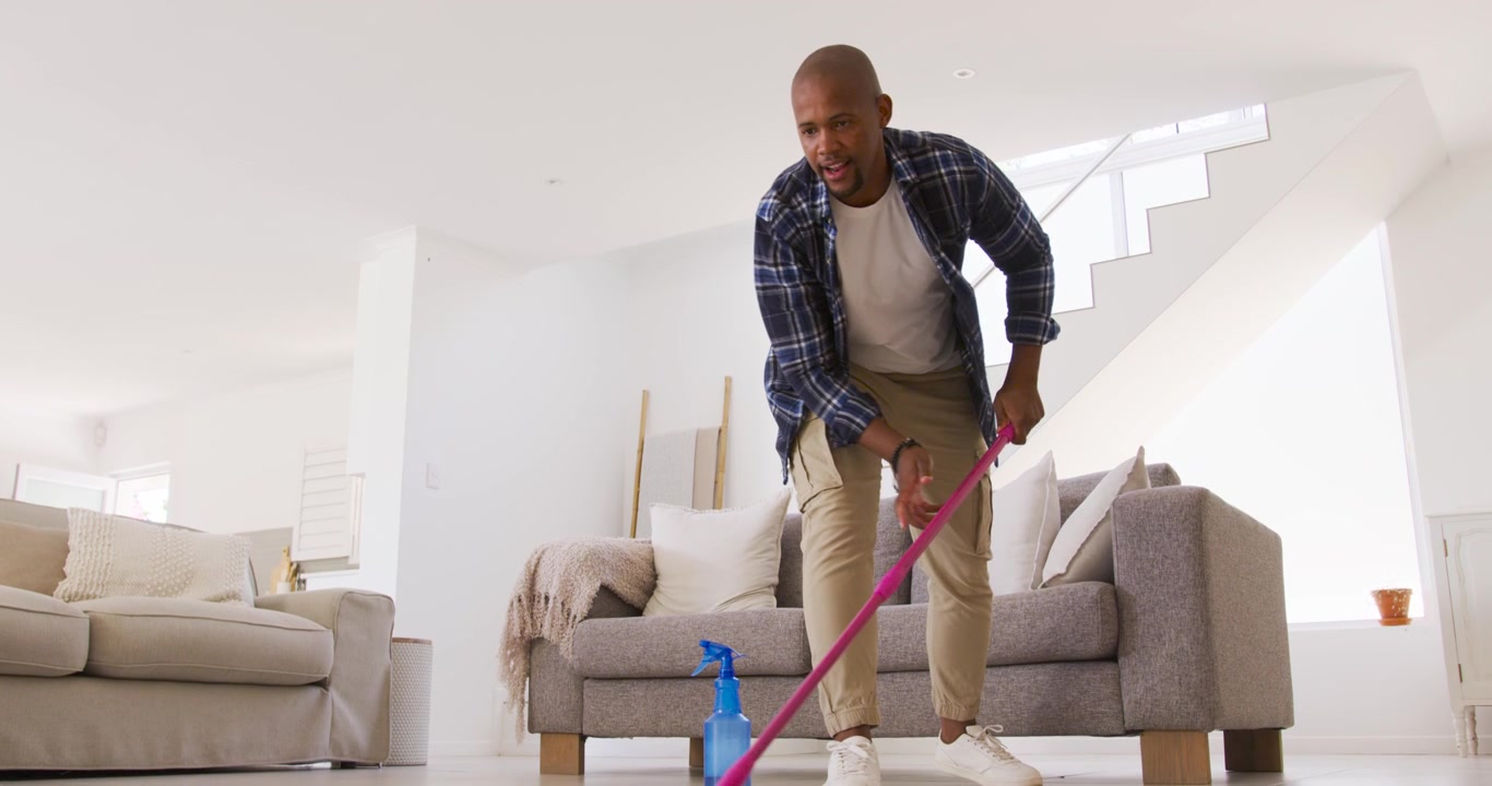 African American man in plaid spraying from blue bottle and mopping with pink mop, cleaning floor