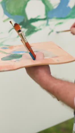 un artista, con un enfoque en su trabajo, se ve sosteniendo una paleta de madera llena de colores de pintura vibrantes. vestido con una camisa a cuadros, el virtuoso está aplicando cuidadosamente pintura a un gran lienzo