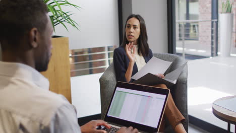 dos personas de negocios diversas enfocadas trabajando juntas, usando computadora portátil en una oficina moderna