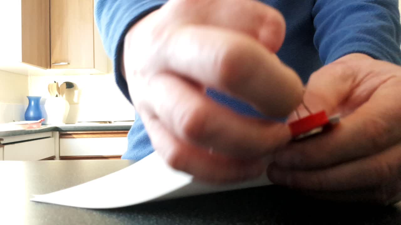 Male with a partially amputated index finger on his right hand putting a red bull dog clip on some white strips of paper