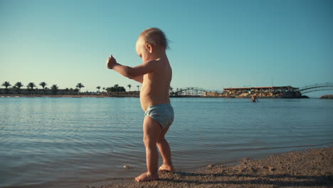 Adorable-baby-boy-sunbathing-at-seaside.-Cute-child-staying-at-summer-beach.