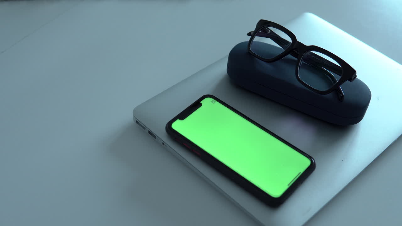 Mobile phone and black glasses on laptop during home office work, white table at home room, pan left to right