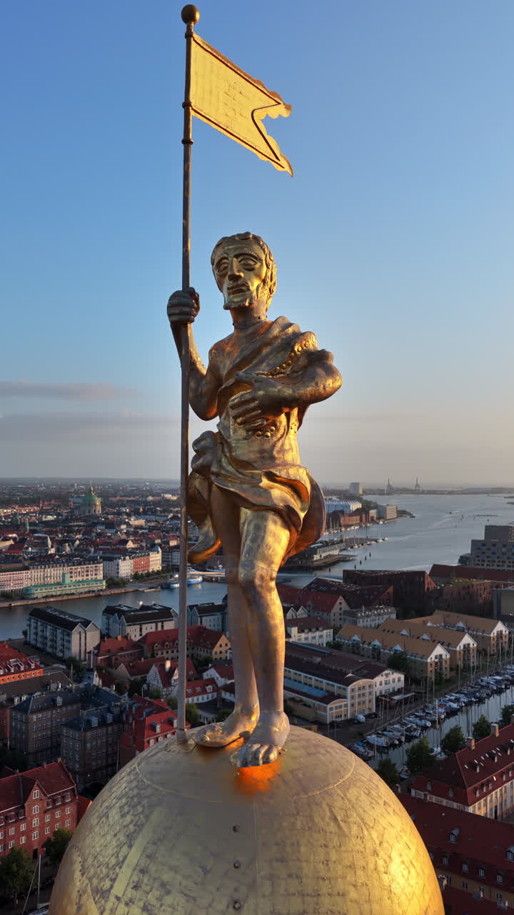 Aerial drone view of the golden statue atop a sphere on the Church of Our Saviour overlooking the Copenhagen skyline, with Frederik's Church dome in the background in Denmark. Vertical