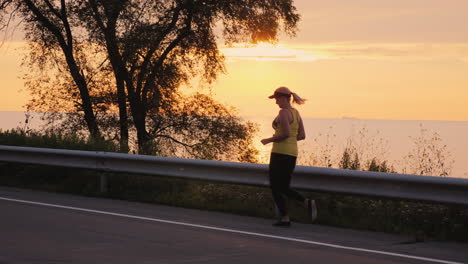 woman makes an evening jog along the road along the lake steadicam follow shot