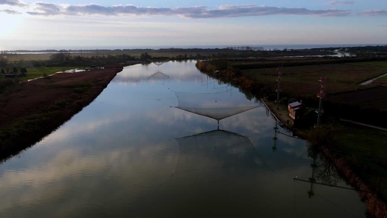 Peaceful morning atmosphere over the Italian countryside. Drone footage capturing the coexistence of traditional river fishing and agriculture along the fertile banks of the Piave