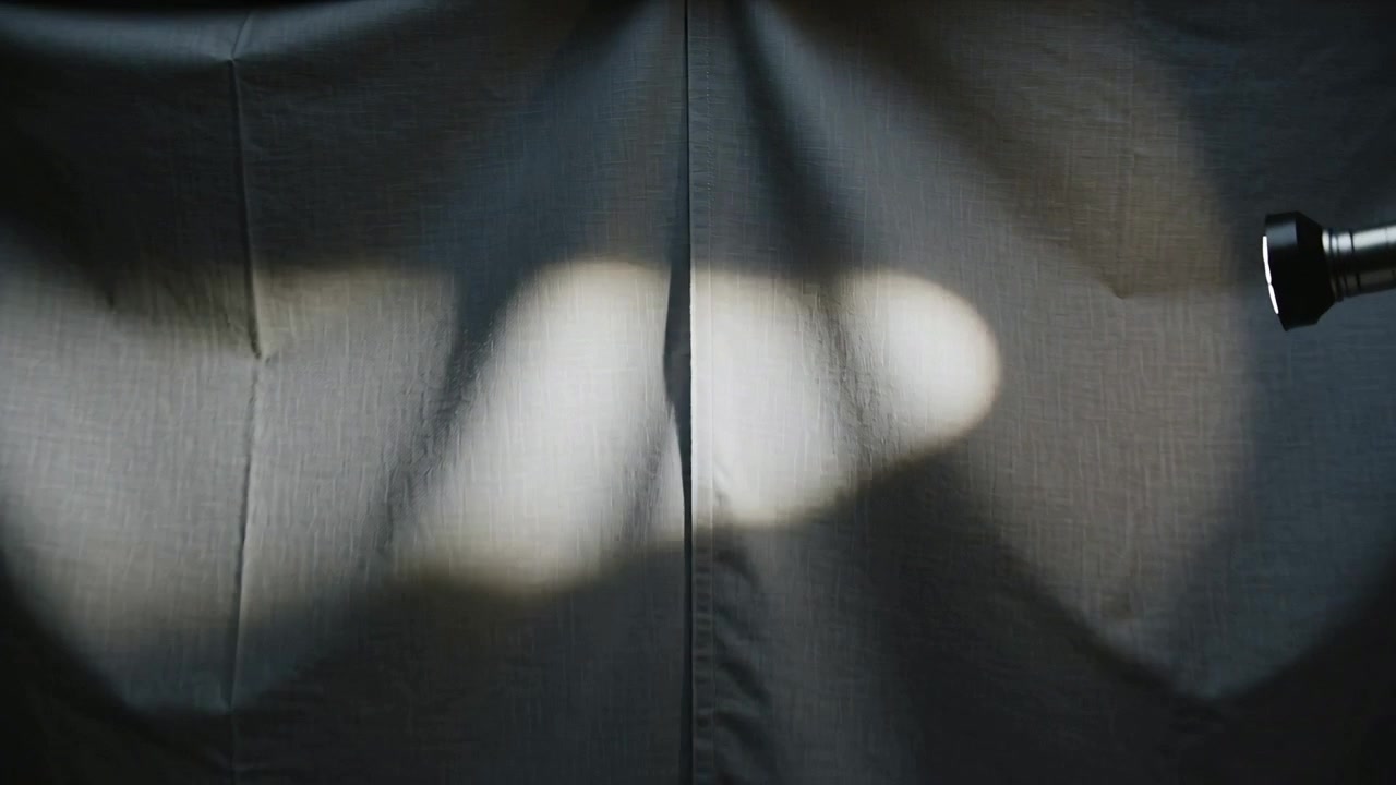 Powering clamped spotlight forming shifting lobed light on dark grey backdrop, shaping fabric seam