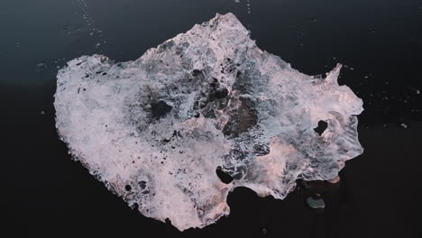 top down close up view of small piece of ice on black sand diamond beach, iceland