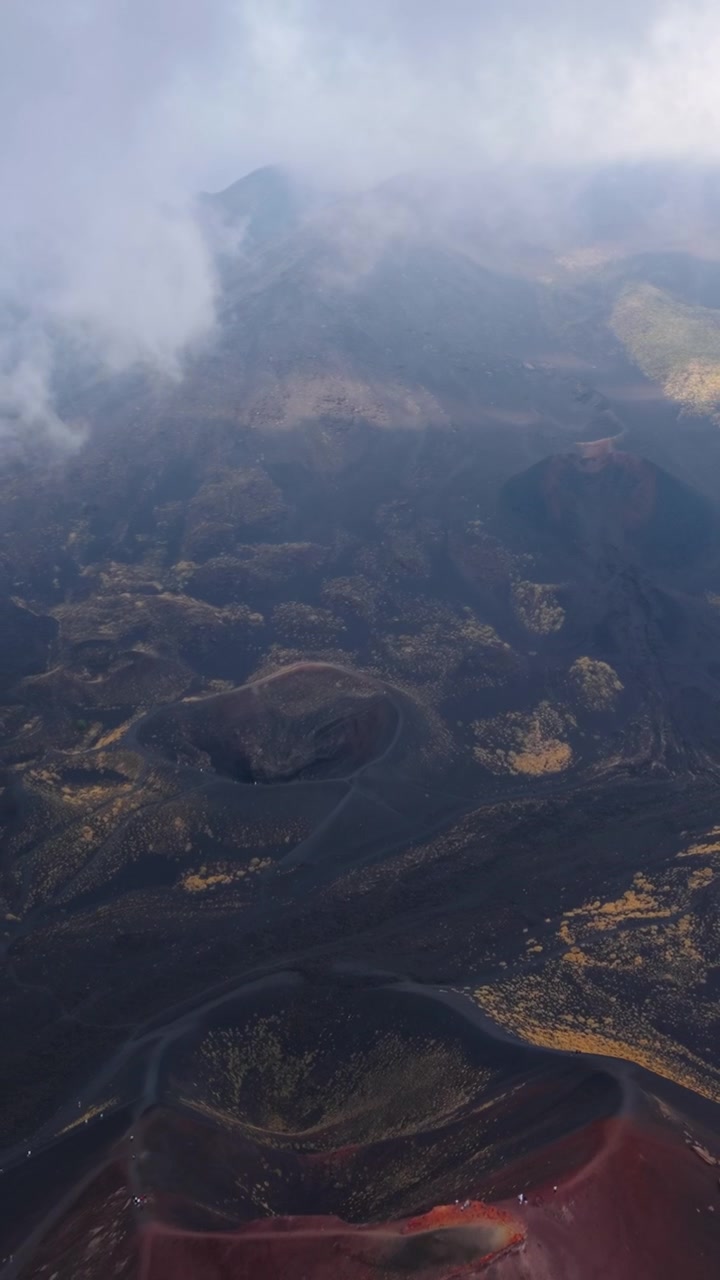 Múltiplas crateras no Monte Etna emergem enquanto o drone recua através das nuvens.