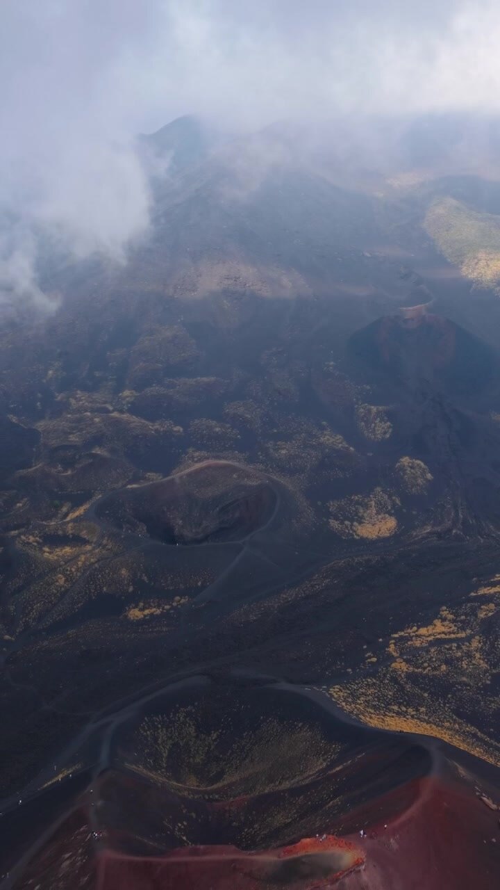 Diversi crateri sull'Etna emergono mentre il drone si allontana tra le nuvole.