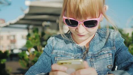 Portrait-Of-A-Blond-Girl-Using-A-Smartphone-Sits-On-A-Summer-Terrace-In-A-Cafe-Bright-Sunny-Summer-V