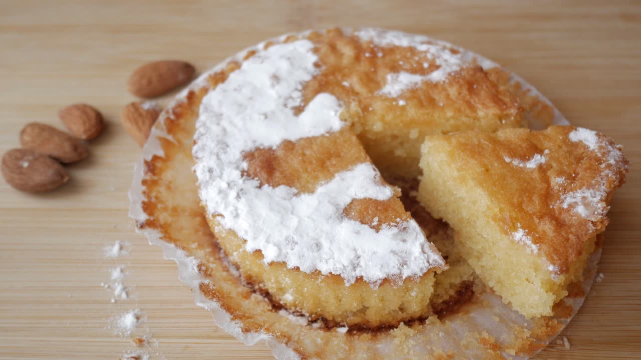 Hand takes a piece of Tarta de Santiago, almond cake, wooden table