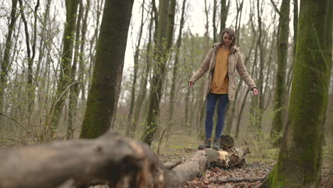 a young girl balances across a fallen tree trunk in the middle of the forest