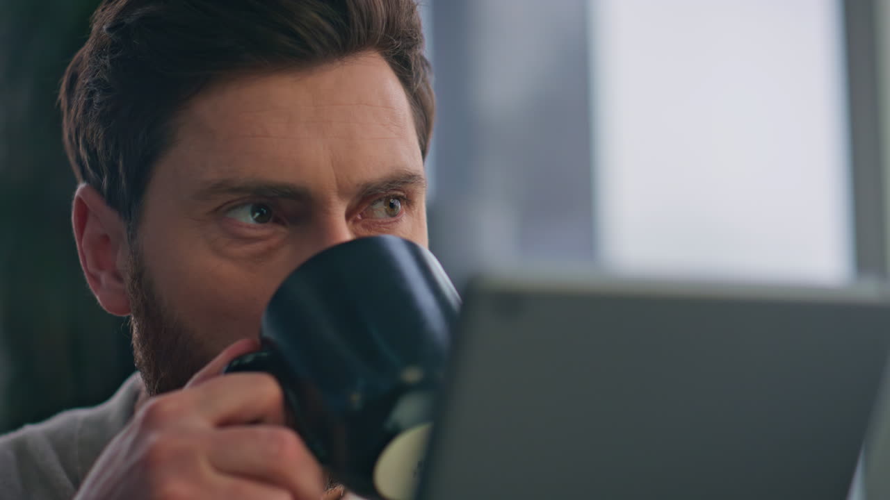 un tipo de primer plano bebiendo café leyendo una tableta en el apartamento de la mañana.