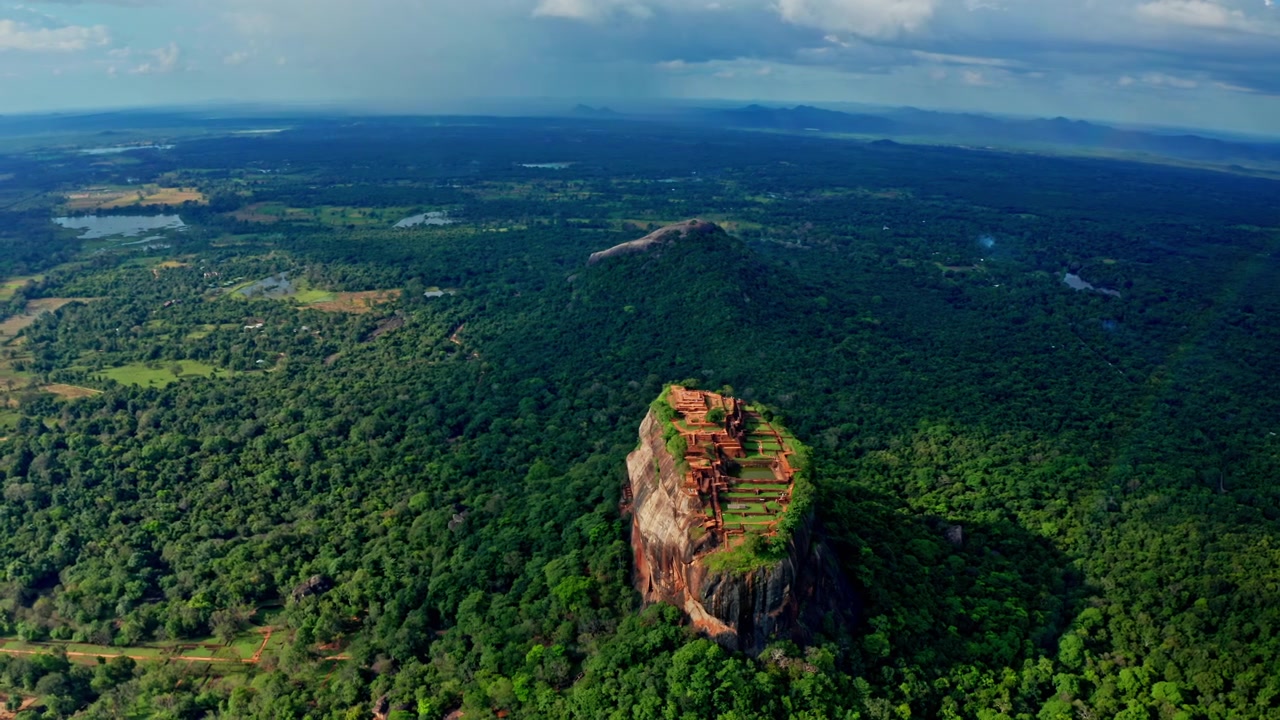 Vista aerea con drone della Roccia del Leone di Sigiriya nello Sri Lanka, con un arcobaleno sopra una giungla lussureggiante, che mostra le antiche rovine della fortezza e paesaggi drammatici.