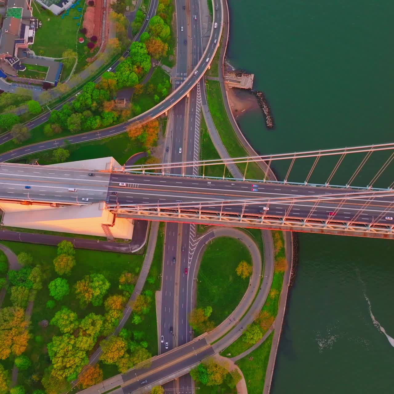 Lively motorways at the bank of the East River. Top view on the bridge, roads, green waterfront and sea-green water