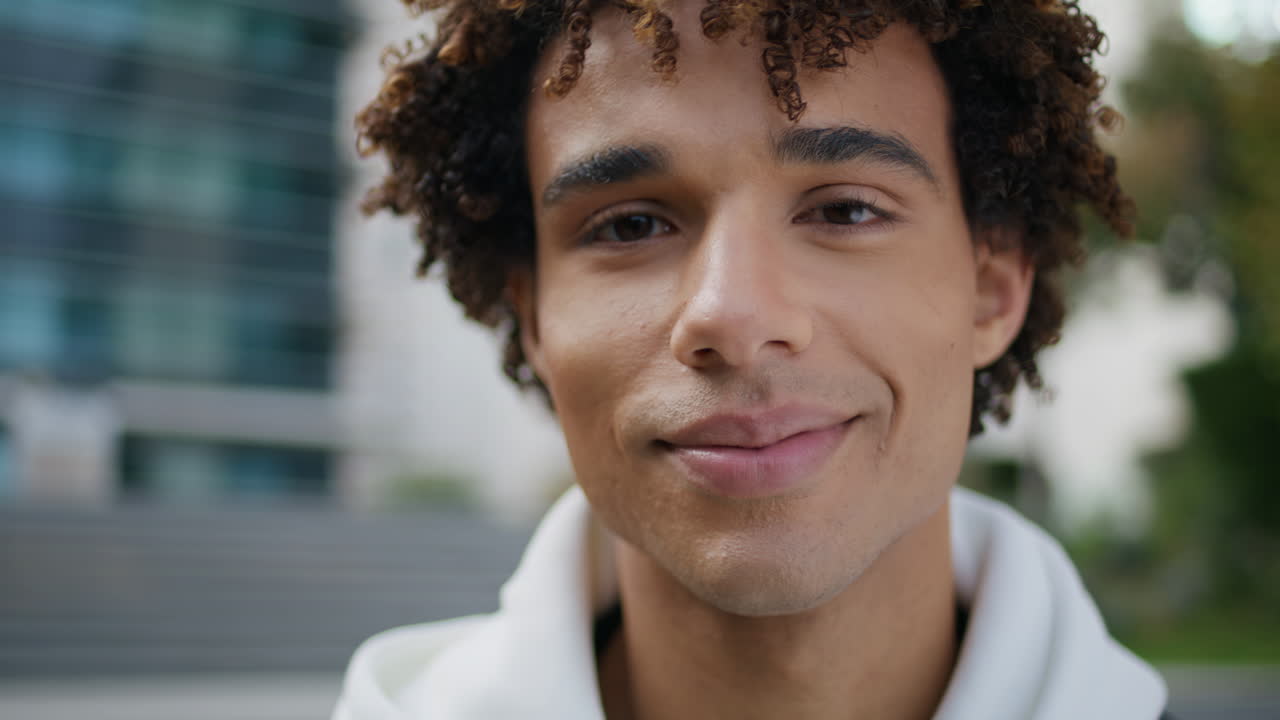 Curly guy face posing city portrait. Young man looking camera smiling on street