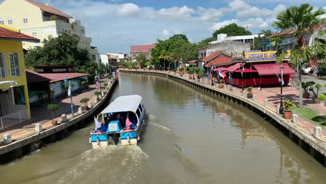 Narrow-looking-Malacca-River-with-houses-while-boat-is-cruising-the-river-and-a-cloudy-blue-sky-in-the-background