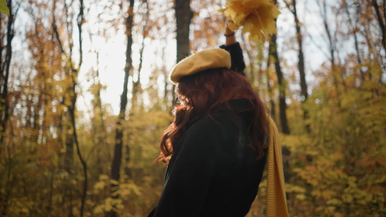 dama alegre con boina amarilla, sosteniendo hojas de otoño, baila en un bosque bañado en la luz del sol, creando una escena mágica y pintoresca rodeada de vibrantes colores de otoño