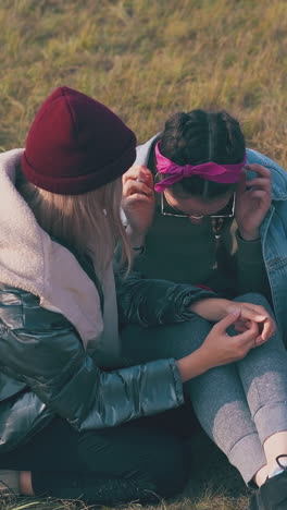 beautiful girls tourists in casual clothes watch video on smartphone sitting on grass in warm autumn evening closeup