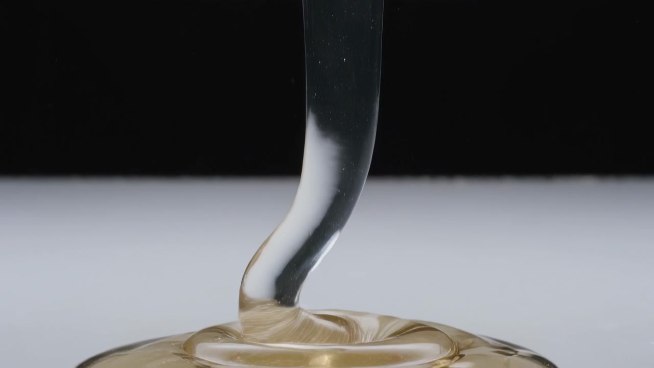 Ugello che rilascia un liquido ambrato, viscoso e traslucido su un piatto bianco, formando una pozzanghera lucida.