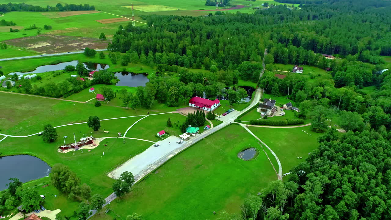 Aerial drone zoom in shot over historic Minhauzena manor in Dunte, Latvia surrounded green grasslands alongside small ponds along rural countryside at daytime