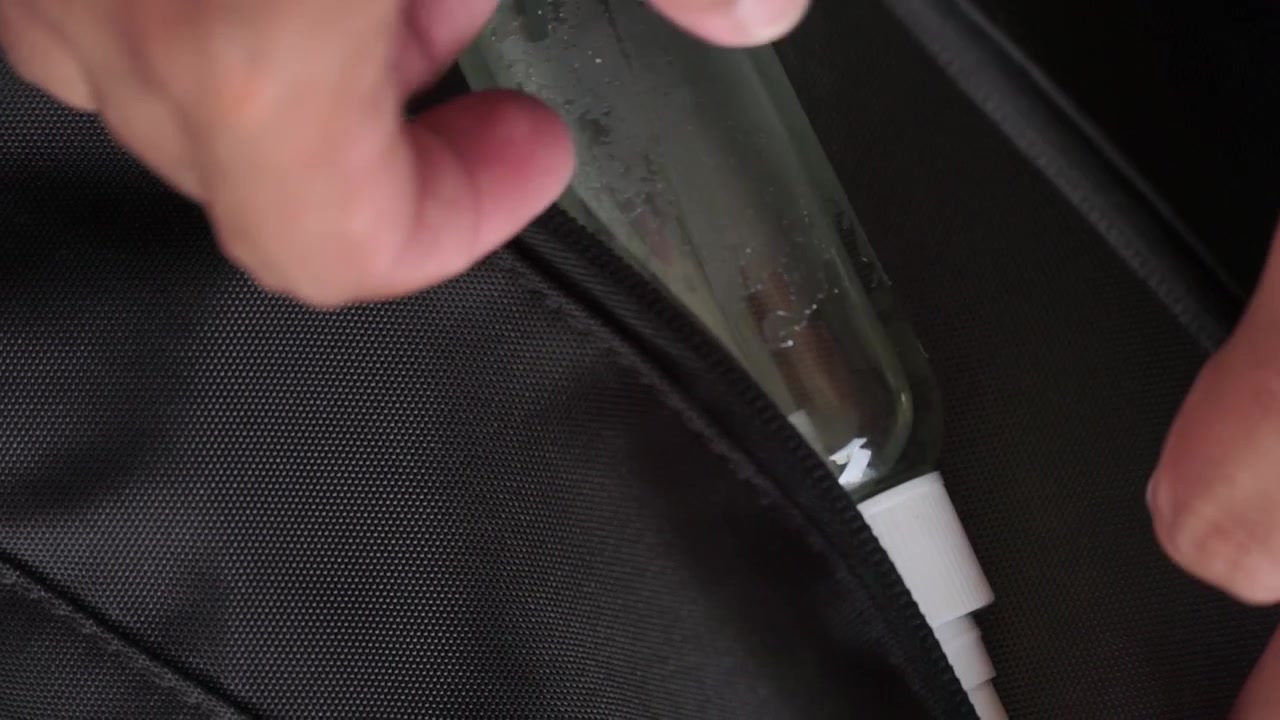 Mano sacando una botella de desinfectante de manos de un bolso con cremallera en primer plano, ideal para conceptos de tecnología, viajes y estilo de vida.