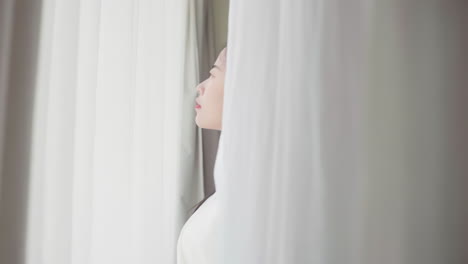 real shot of beautiful girl getting up in white pajamas waking up in her bed sitting near the big window fully rested and open the curtains stretching in the morning to get fresh air and sunshine